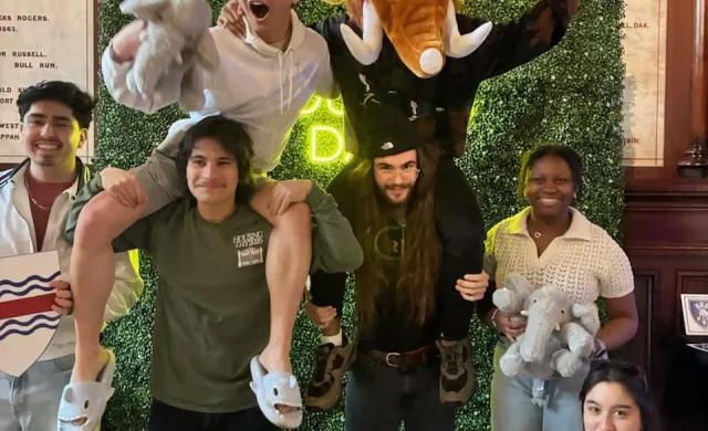 A group of first-years taking pictures in front of a housing day backdrop in Memorial Hall