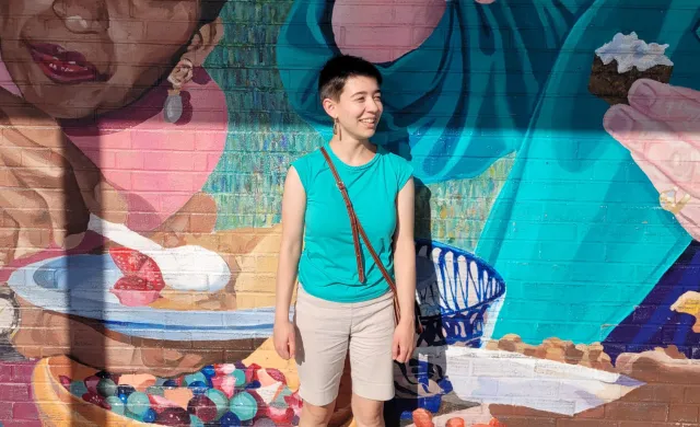 A student stands in front of a colorful mural