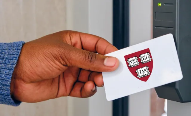 A hand holding a card featuring a Harvard ID with the Harvard crest