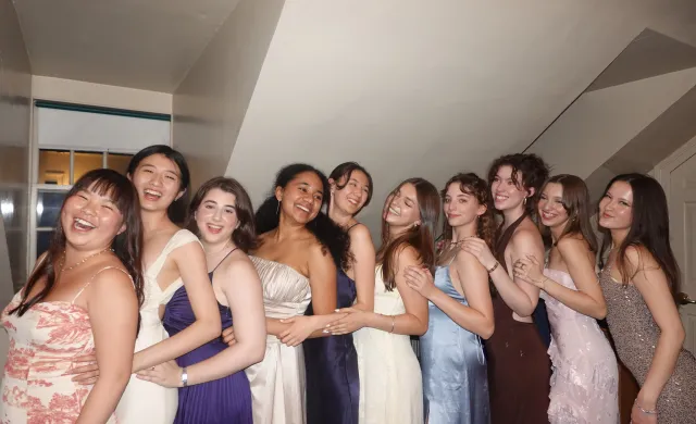 Group of ten girls in formal dresses, lined up and laughing 