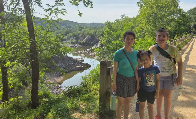 Three siblings stand in front of an overlook that looks down on a river.