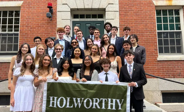 A diverse group of first-year students gather for a group photo in front on their house in formal attire
