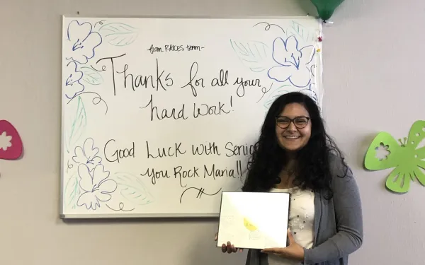 Maria posing in front of a farewell message at the end of her internship. 