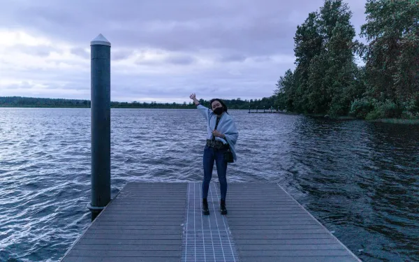 I am posing happily by a lake in my hometown near Seattle, WA. It's really cloudy and getting dark. 