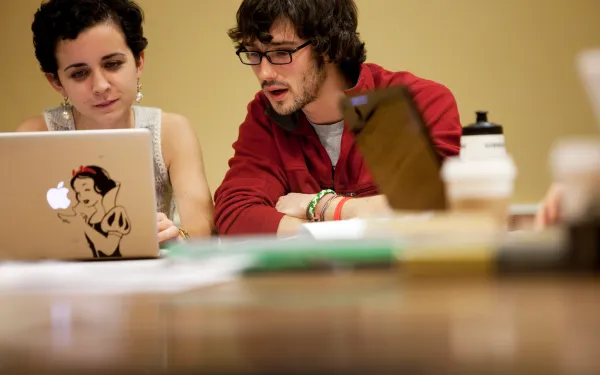 Two students sharing a laptop and speaking to one another