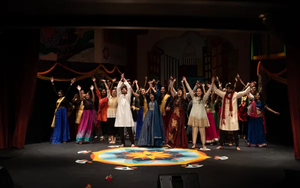 Students wearing South Asian clothing all preparing to bow on stage in the finale of Harvard Ghungroo 2020, with a Rangoli set in front of them.