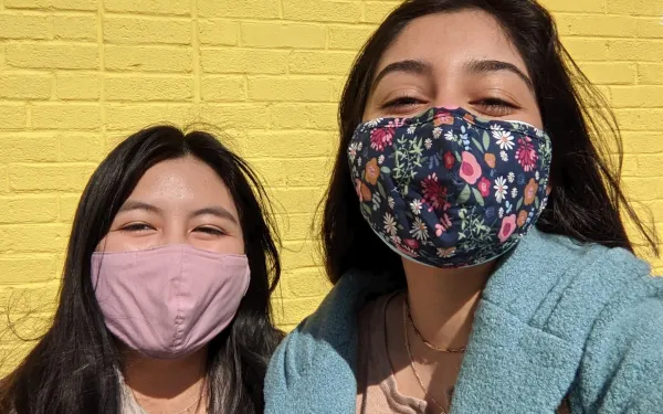 Two girls standing in front of a yellow wall.