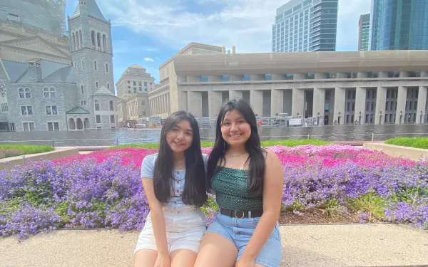 Two girls sitting by flower beds.