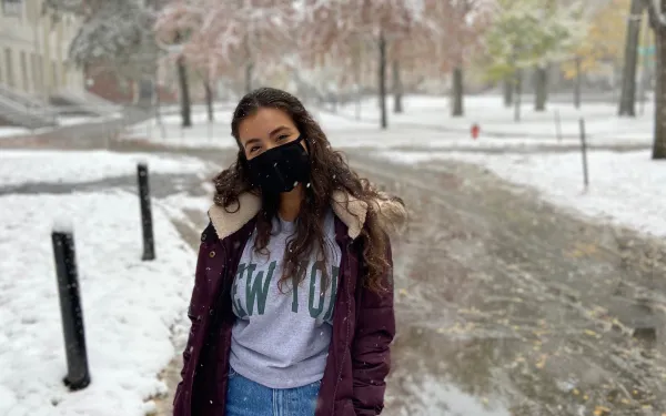 Girl in a big dark red coat in a park while it is snowing. 