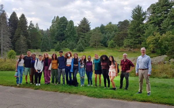 Group picture of students and professors standing beside a road with trees in the background.