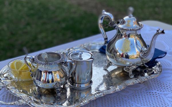 A picture of a silver teapot, creamer pitcher, sugar container, and bowl of lemons on a silver platter.
