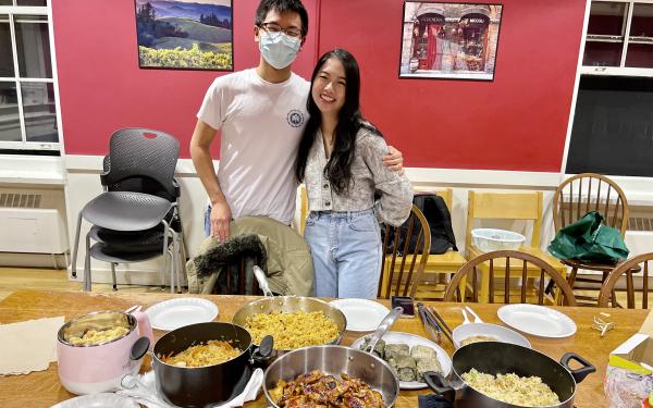 Janny and Raymond standing in front of a table covered in plates and pots with food.