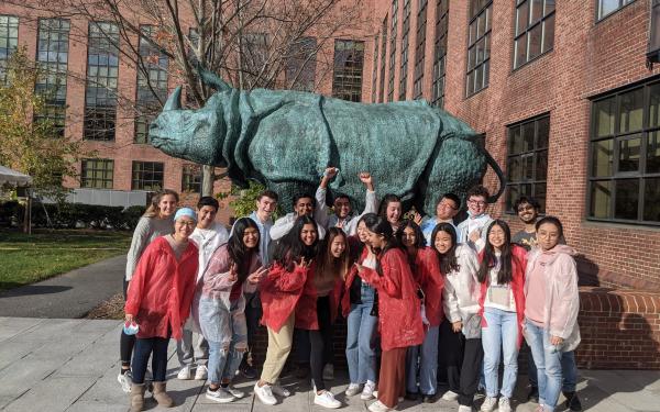 Students in white and red lab coats standing in front of a rhino statue.