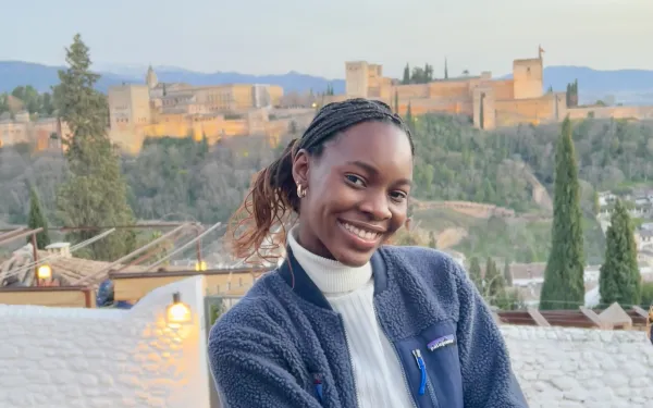 Writer smiling in front of Granada's Alhambra, a castle-like structure on the horizon.