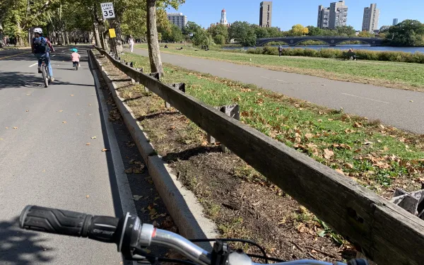 Picture of a grassy walkway beside a river with buildings in the background.