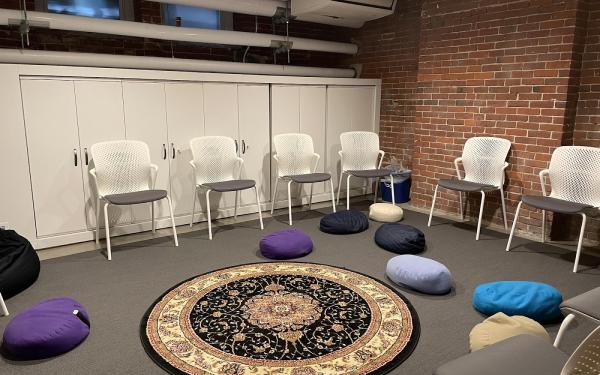 A photo of an office set up with six white chairs organized in a circle, and a rug on the floor in the middle surrounding my colorful bean bags.