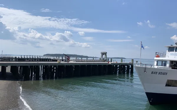 Picture of pier stretching out into the ocean with a white boat coming in.