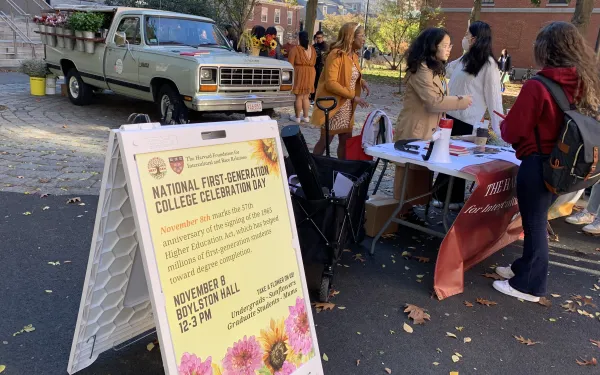 Picture of "National First-Generation College Celebration" sign with students and a truck in the background.