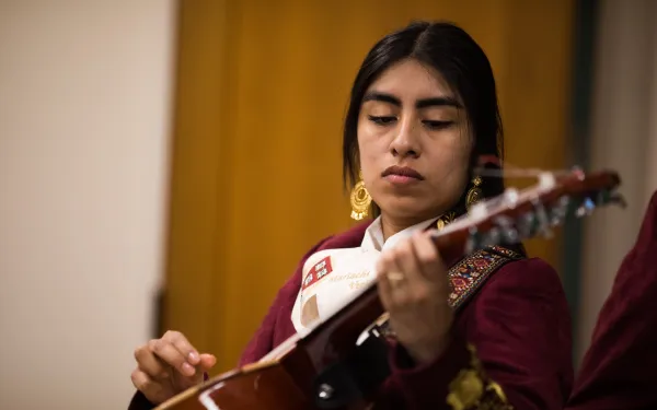 A female mariachi musician holds her instrument while wearing her mariachi suit