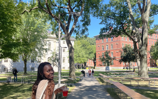 Author walking through Harvard Yard with hibiscus drink, smiling. 