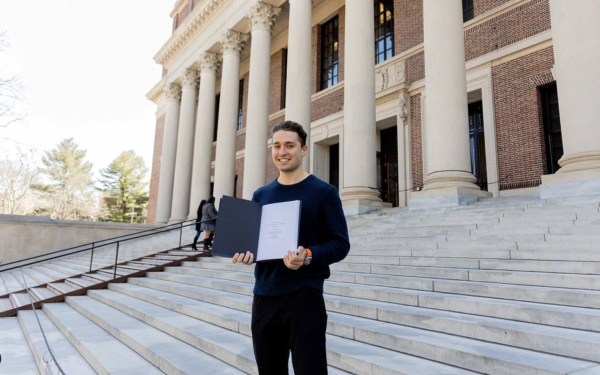 Students holds thesis book on stairs of Widener Library