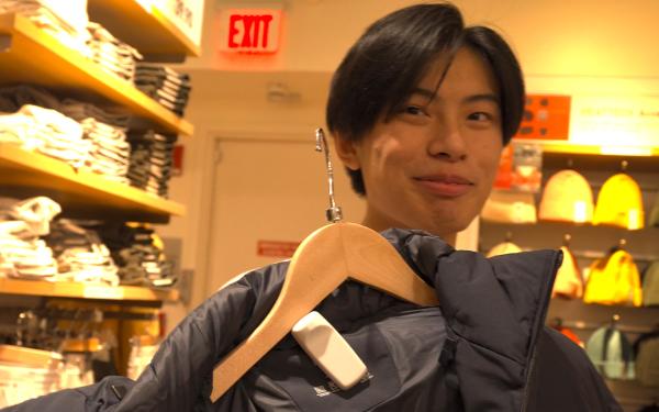 A student holding a winter coat at a clothing store.