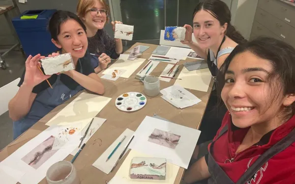 Four students smiling and surrounding a table with artworks