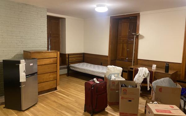 A picture of a room during move in day, with suitcases and boxes along with the furniture. The room, undecorated, looks new.