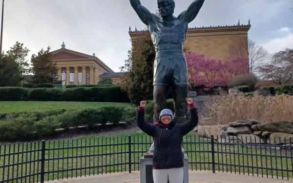 Merlin standing in front of Rocky Statue with fists in the area in front of the steps where the Rocky movie scene was shot