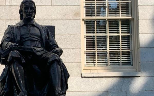 This is a picture of the top of the John Harvard Statue, which shows only the shape of the statue itself, and not the base with it's description. The statue shows a man posing in a sitting, very academic looking, position. 