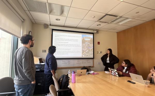 Students sitting and standing around a table looking at a presentation