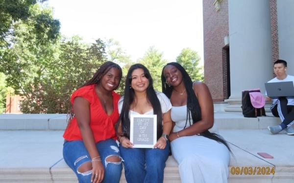 My friends and I sitting on the steps of Widener Library, holding a sign that says "Happy First day of 14th Grade"."
