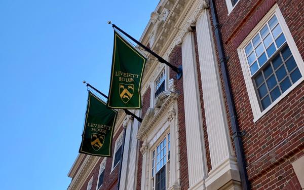 A brick building with two green "Leverett House" flags and white columns under a clear blue sky