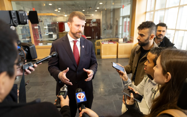 Man in suit speaking to reporters with microphones in hand