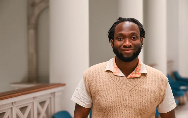 Hassan smiles while standing in a classroom hallway.