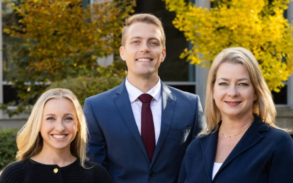 Three people in business attire smiling outdoors.