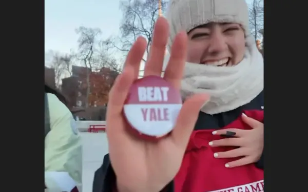 Person in winter clothes smiles and holds up a "Beat Yale" button.