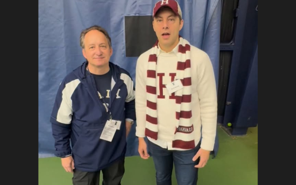 Two men standing side by side, one in Yale gear and the other in Harvard gear, indoors.