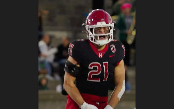 Harvard football player in black and red uniform celebrating on the field.