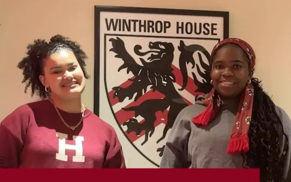 Two Winthrop House students stand smiling in front of a Winthrop House crest sign.