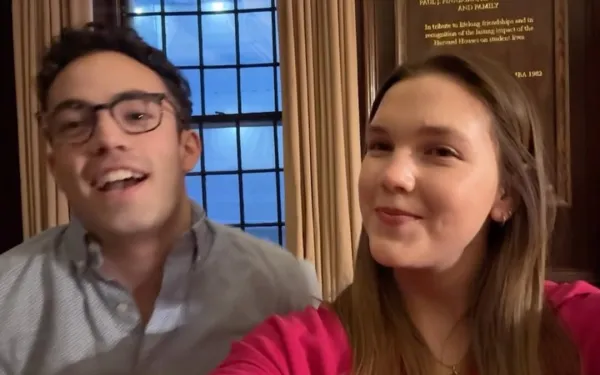Two Adams House students smile indoors in front of a window