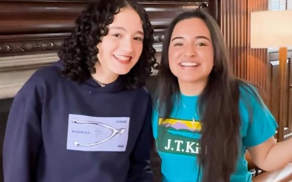 Two students stand smiling in front of ornate dark wood paneling