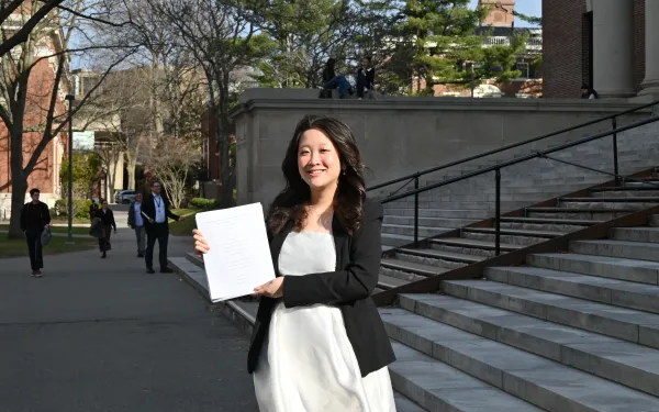 Lani Tran '26 standing on the steps of Widener library holding her thesis pages.