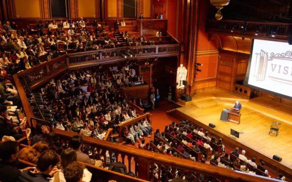 A lecture held in Sanders Theater with the word VISITAS projected onto a screen.