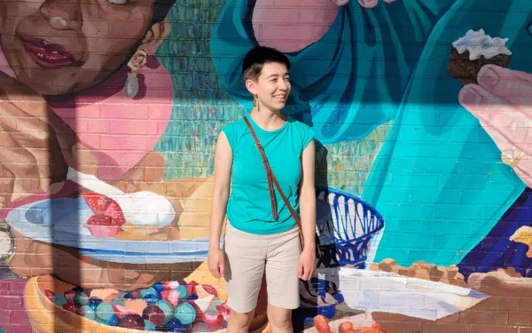 A student stands in front of a colorful mural