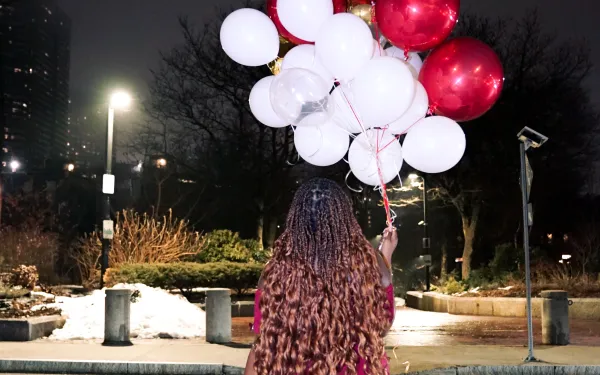 Photo of girl in red dress holding red and white balloons while walking across the street
