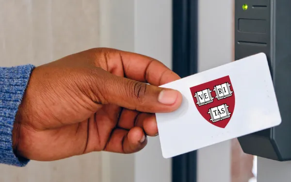 A hand holding a card featuring a Harvard ID with the Harvard crest