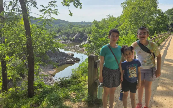 Three siblings stand in front of an overlook that looks down on a river.